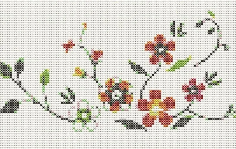 Une main tient un tambour à broder en bois avec une petite broderie florale en point de croix, échevette de coton et ciseaux fins posés à côté